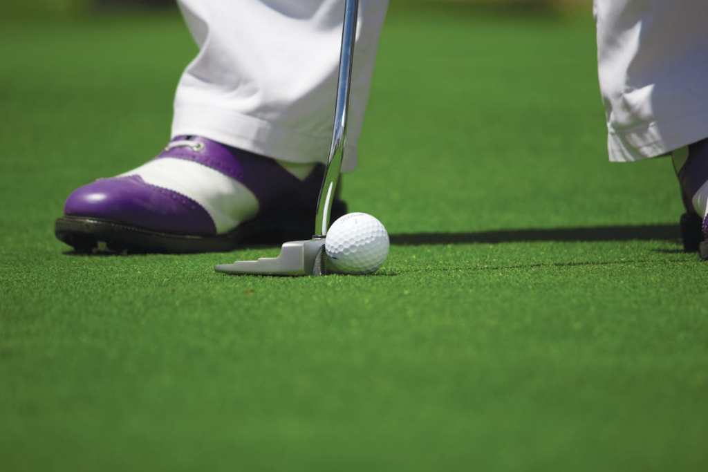 Golfer’s club hitting a white ball on the green
