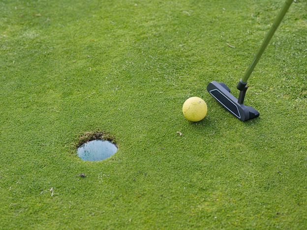 A golf ball and putter near the hole 