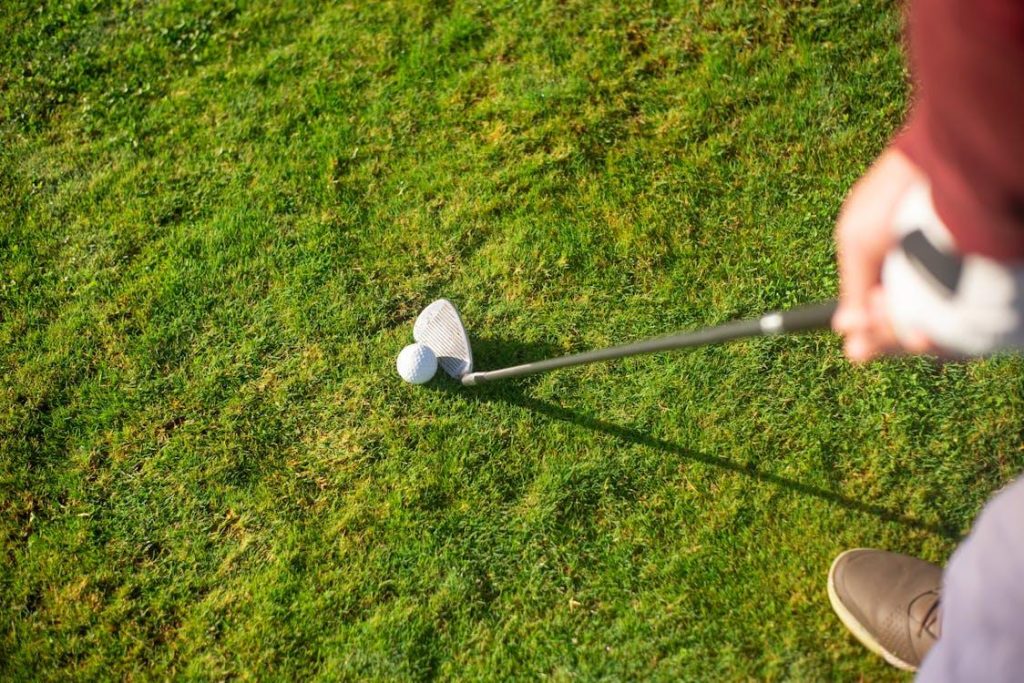 A person holding the golf club next to the ball
